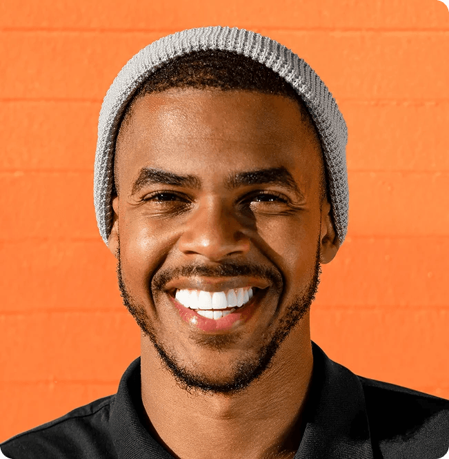 A smiling man in a grey beanie against an orange wall